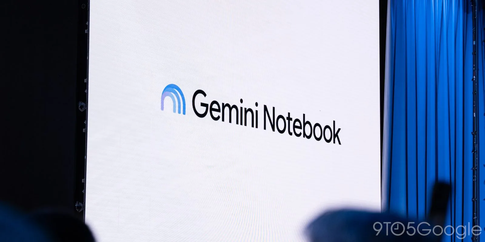 The Gemini Notebook logo on a big screen on a stage, beside a blue curtain.